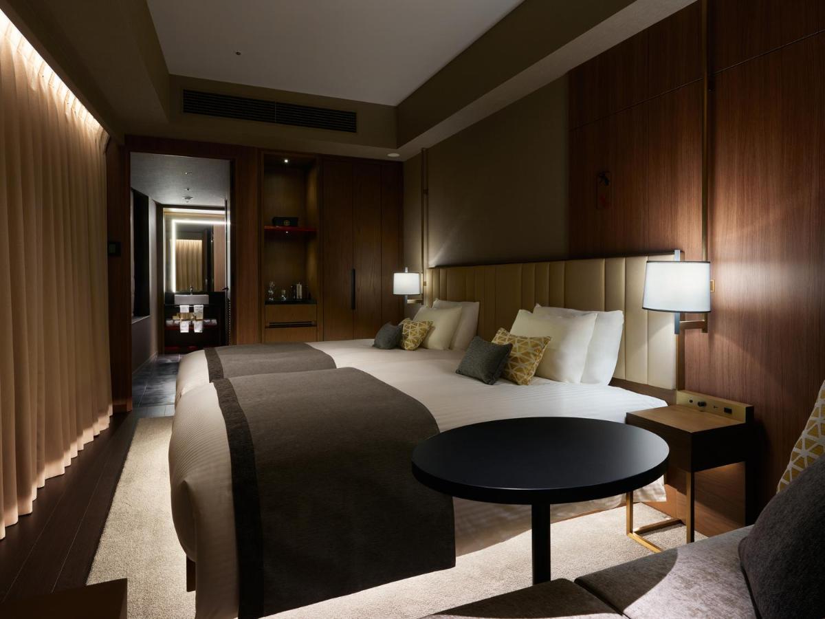 Mitsui Garden Hotel Roppongi Tokyo Premier Esterno foto The photo shows a stylish hotel room featuring two beds with plush bedding and decorative pillows. The walls are made of wood, creating a warm and modern atmosphere. There are bedside lamps on each side of the beds providing soft lighting. A small ro