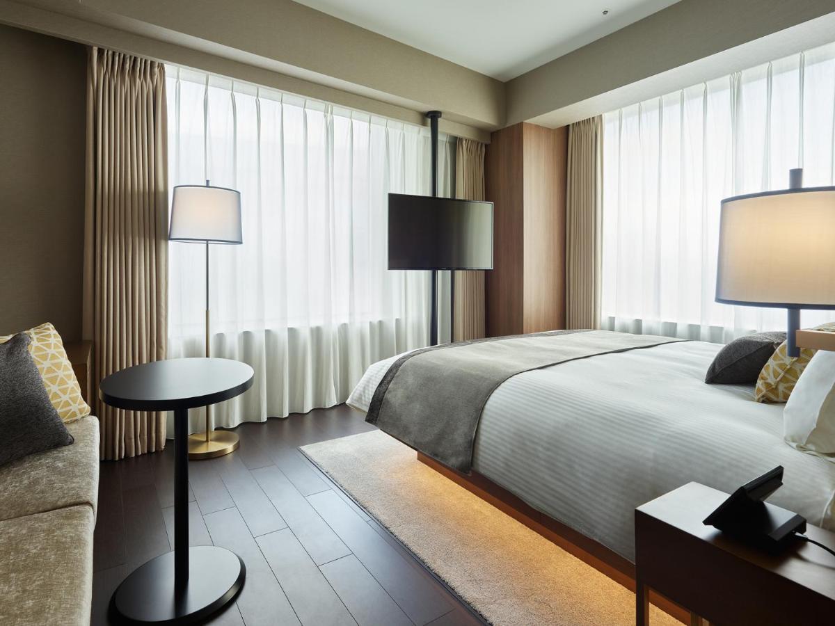 Mitsui Garden Hotel Roppongi Tokyo Premier Esterno foto The photo shows a modern hotel room with a contemporary design. It features a large bed with crisp white linens, sitting against a wall with floor-to-ceiling windows covered by sheer curtains, allowing natural light to filter in. To the side, there's