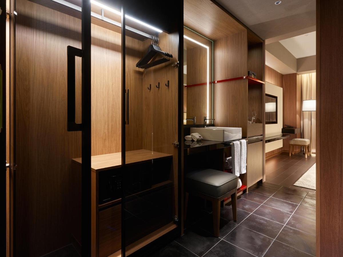 Mitsui Garden Hotel Roppongi Tokyo Premier Esterno foto The photo depicts a modern and stylish hotel room's closet area. It features wooden cabinetry with a sleek finish, including mirrored doors. Inside, there are hangers for clothing and hooks mounted on the wall. A small bench or chair is positioned ne