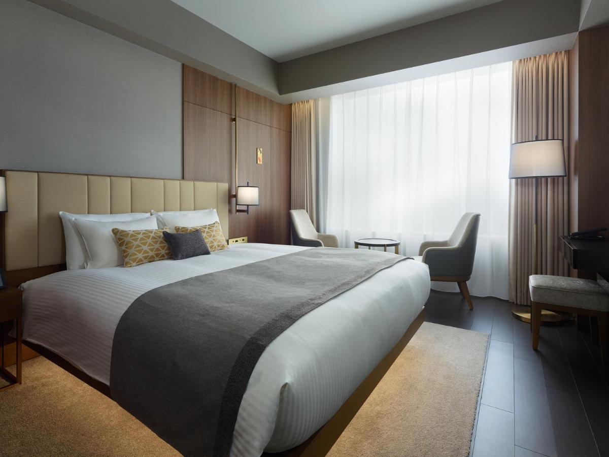 Mitsui Garden Hotel Roppongi Tokyo Premier Esterno foto The photo shows a modern hotel room featuring a large bed with a neatly arranged white and gray bedding. The headboard is upholstered in a light color, adding to the room's contemporary design. On either side of the bed, there are bedside lamps provi