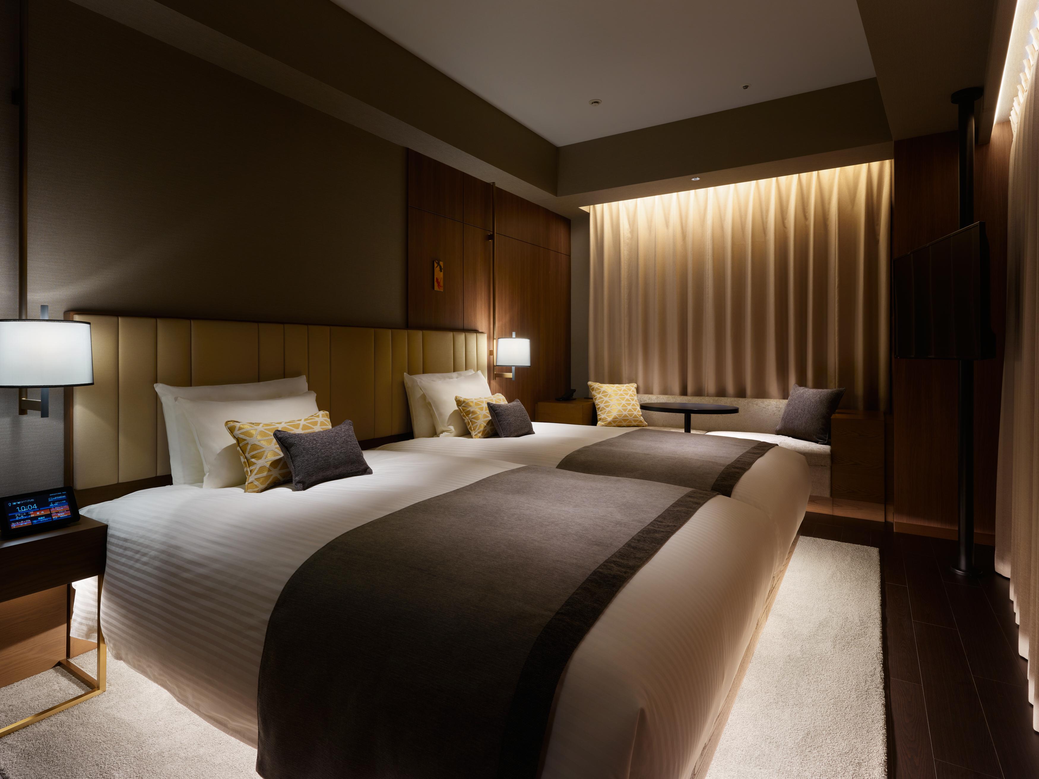 Mitsui Garden Hotel Roppongi Tokyo Premier Esterno foto The photo shows a modern hotel room featuring two beds with plush white linens and decorative pillows. The room has a warm and inviting ambiance, highlighted by soft lighting from lamps and the backlit curtains. There is also a small table with chair