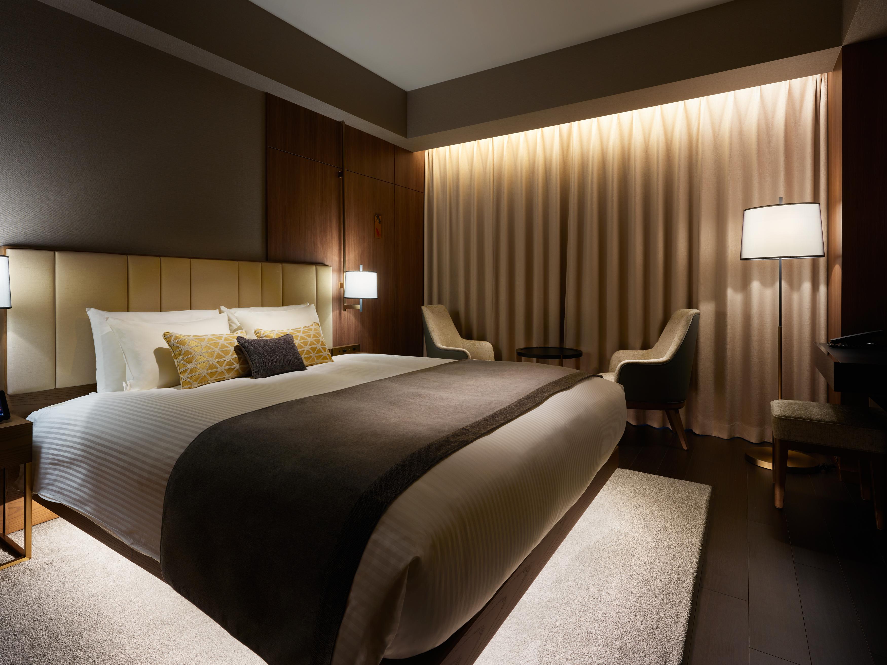 Mitsui Garden Hotel Roppongi Tokyo Premier Esterno foto The photo depicts a modern hotel bedroom. It features a large bed with white linens and a dark gray throw blanket, accented by decorative pillows. The room has a warm ambiance created by soft lighting, including two bedside lamps and a lighted area b
