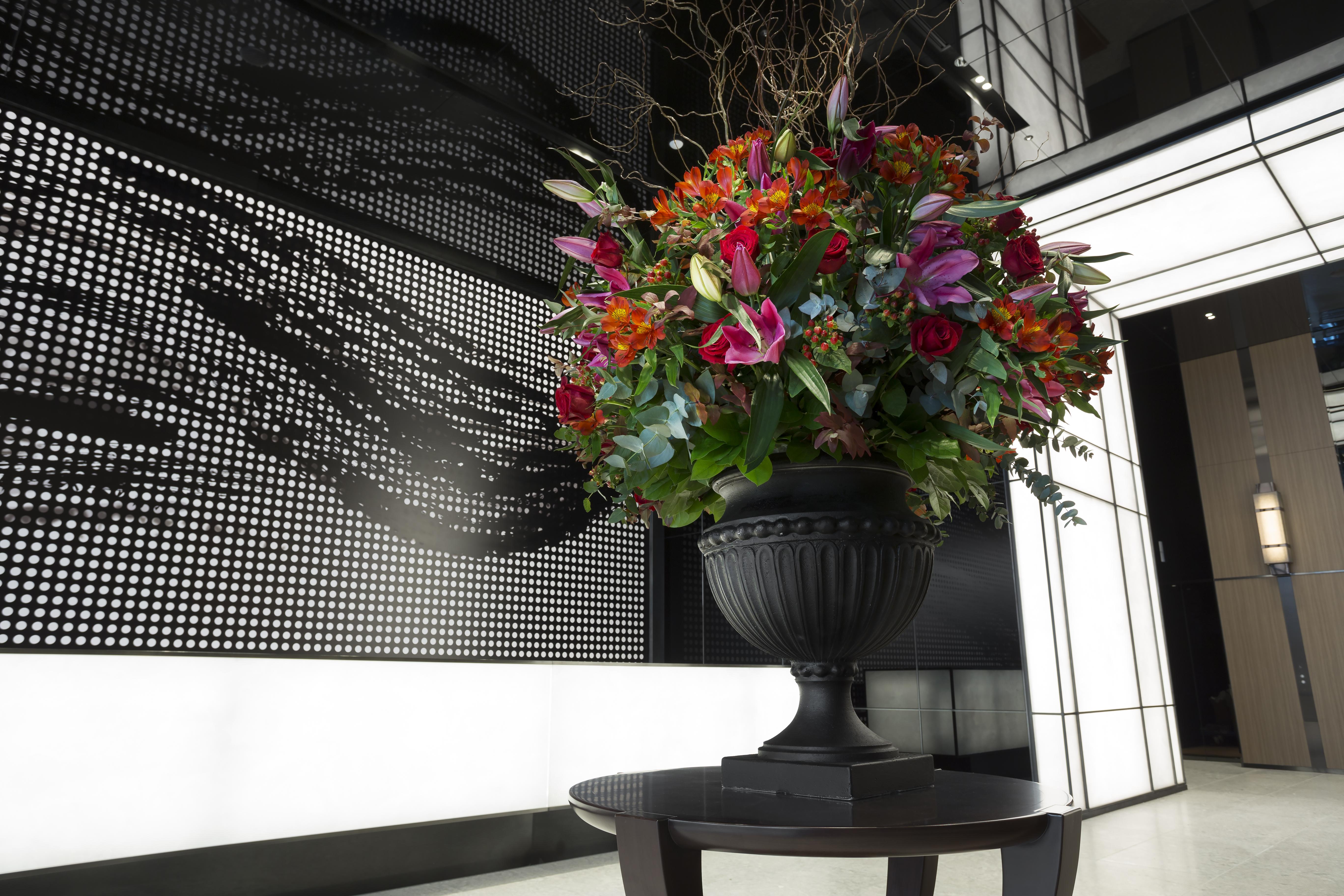 Mitsui Garden Hotel Roppongi Tokyo Premier Esterno foto The photo features a large, vibrant floral arrangement in an ornate black urn. The arrangement is composed of various colorful flowers and greenery, showcasing shades of red, pink, orange, and green. This floral display is positioned on a small table