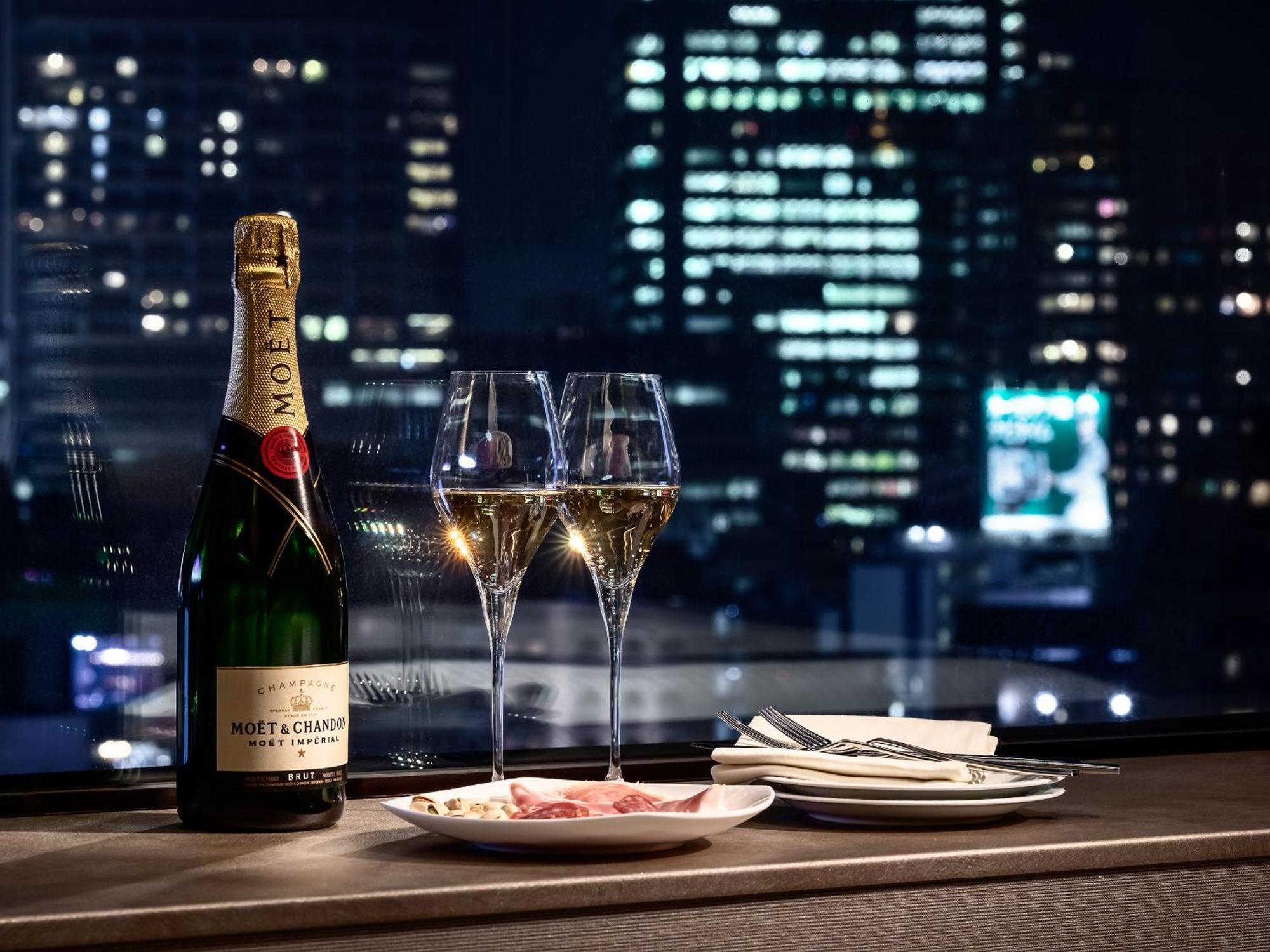 Mitsui Garden Hotel Roppongi Tokyo Premier Esterno foto The photo features a bottle of champagne, specifically Moët & Chandon, alongside two filled champagne glasses. The table setting includes a small plate with a selection of food and neatly arranged utensils. In the background, there is a view of a cit