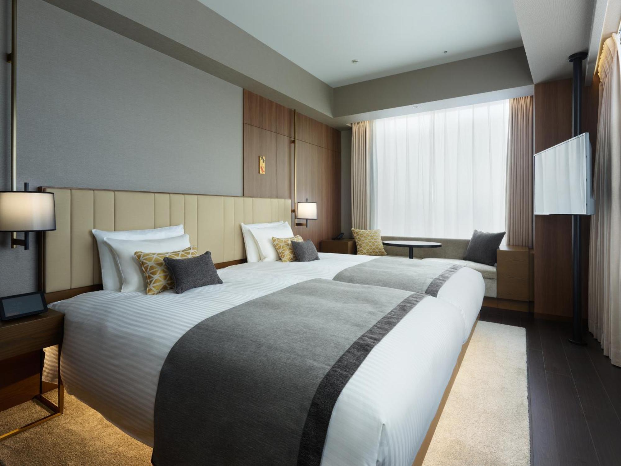 Mitsui Garden Hotel Roppongi Tokyo Premier Esterno foto The photo shows a modern hotel room featuring two beds with white linens and decorative pillows. The room has a minimalist design, with neutral-colored walls and wooden accents. Natural light comes in through large windows, which are partially covere