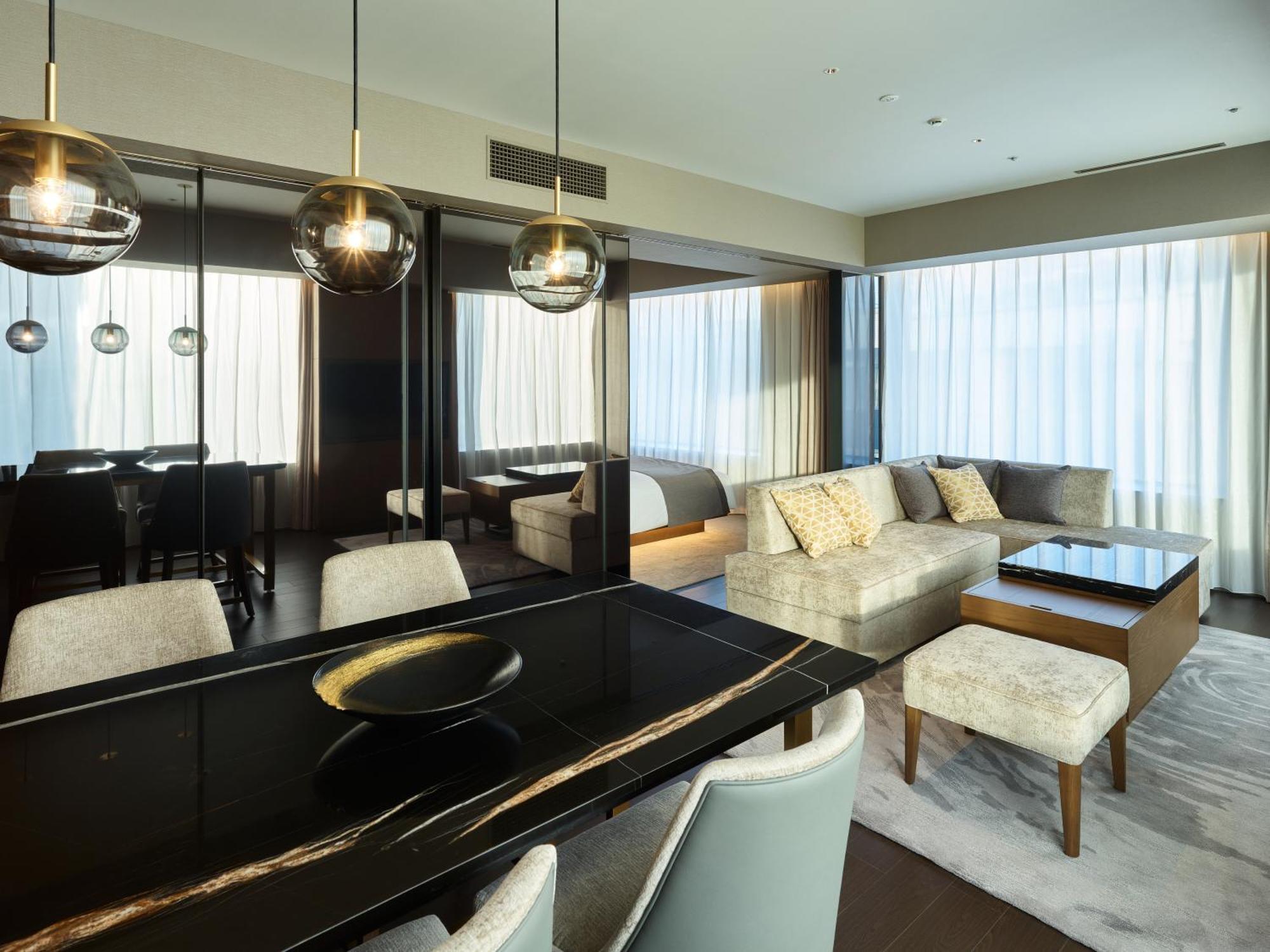 Mitsui Garden Hotel Roppongi Tokyo Premier Esterno foto The photo shows a modern and stylish living area. It features a dining table with elegant chairs, a comfortable seating area with a light-colored sofa, and a coffee table. The room is well-lit by large windows draped with sheer curtains, allowing nat