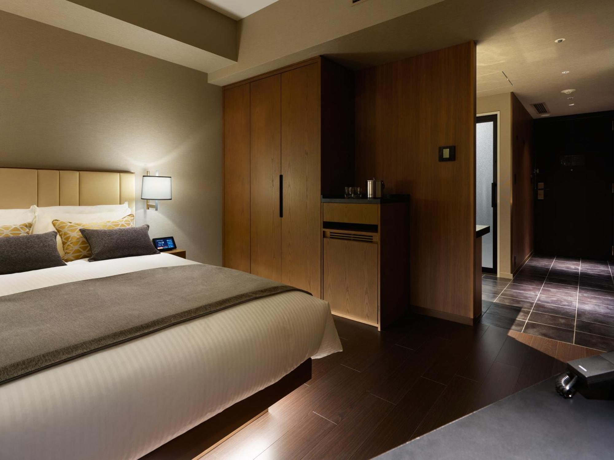 Mitsui Garden Hotel Roppongi Tokyo Premier Esterno foto The photo shows a modern hotel room featuring a neatly made bed with decorative pillows. The room has wooden accents, including a wardrobe and cabinetry, contributing to a warm ambiance. A bedside lamp is on one side of the bed, and there's a small a