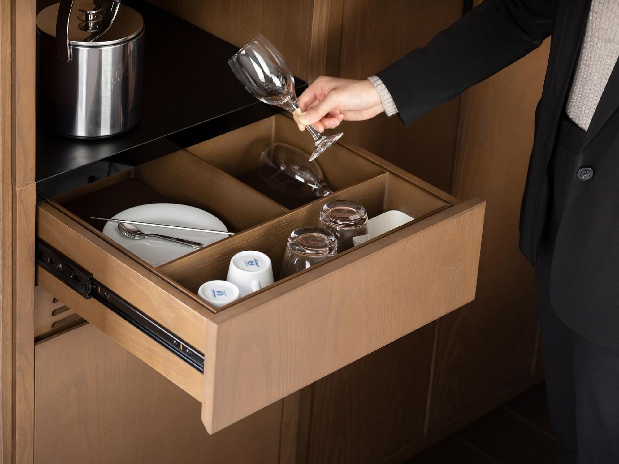 Mitsui Garden Hotel Roppongi Tokyo Premier Esterno foto The photo depicts a wooden kitchen drawer being pulled open, revealing a neatly organized selection of dishware. Inside, there are glass cups, a wine glass being held by a person, and plates. The setting appears modern and sleek, with a sophisticated